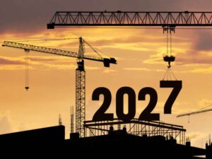 Bouwkranen bij zonsondergang die het jaartal 2027 op een nieuwbouwproject hijsen