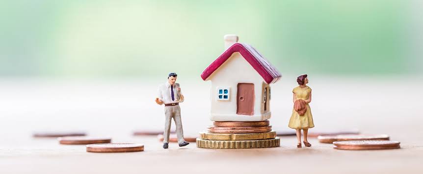 Miniatuurhuisje op stapels munten met twee poppetjes ernaast, symbool voor hypotheek bij scheiding
